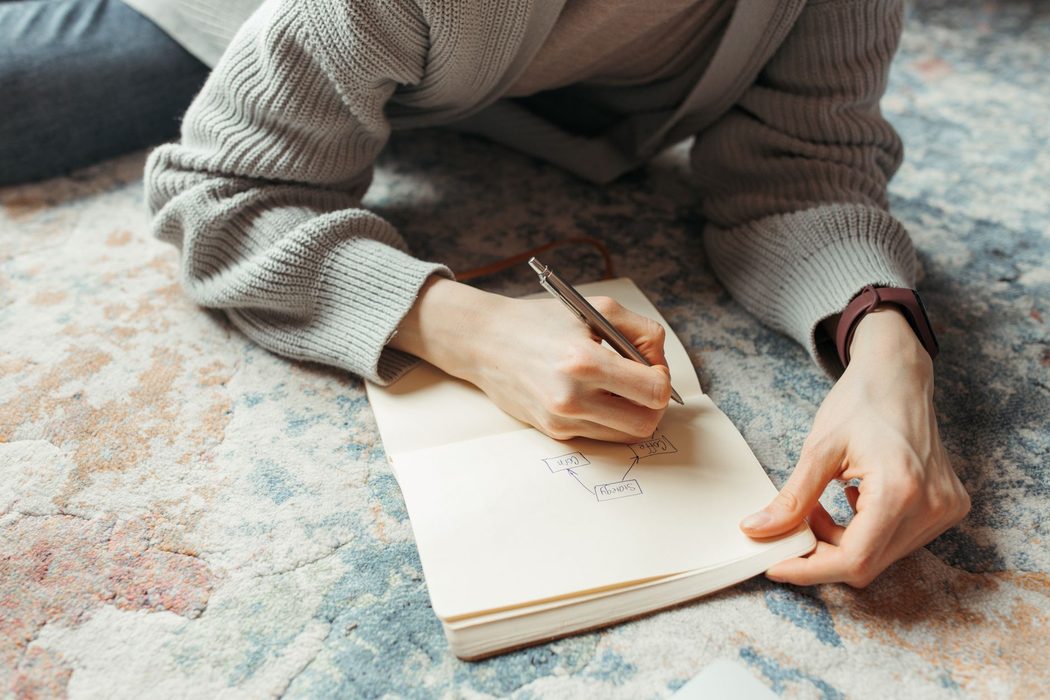 A person sketching a simple boxes-and-arrows diagram on paper beside a notebook